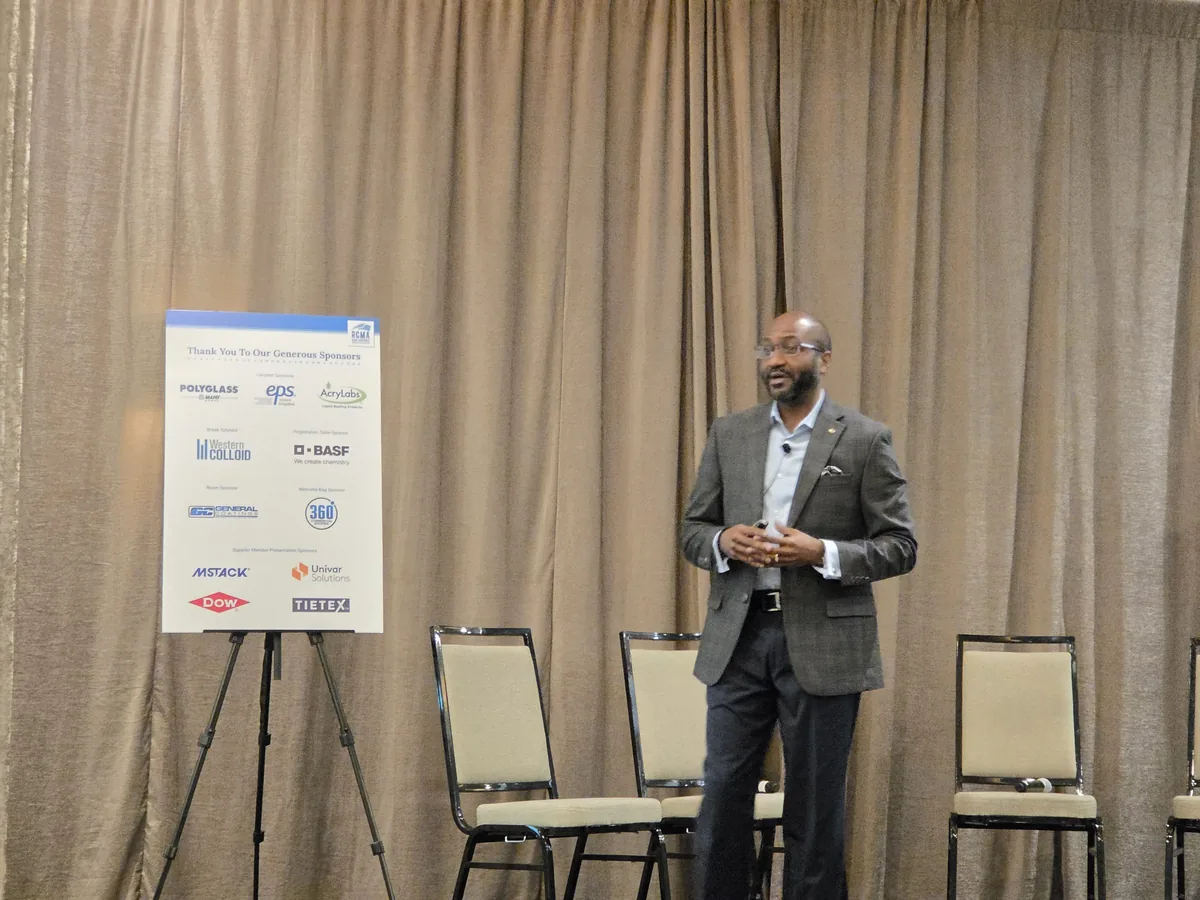 A presenter speaking beside the sponsor board at the RCMA 2026 Fall Meeting.